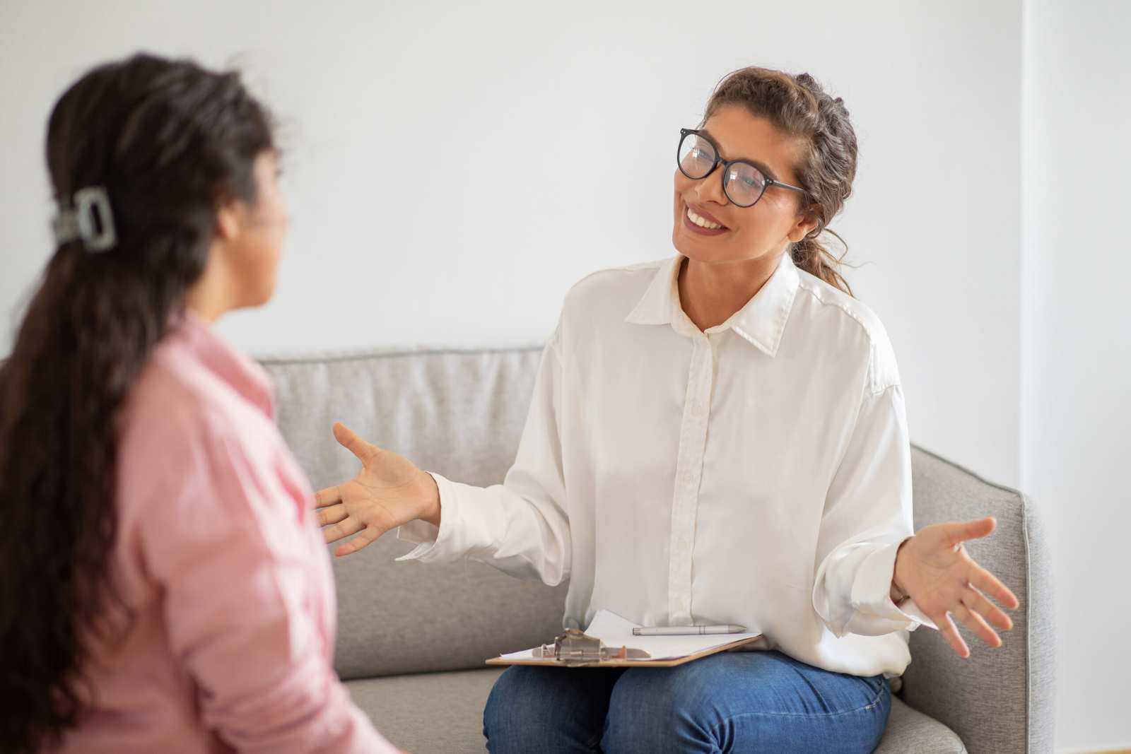 Healmind therapist in kerala , wearing glasses and holding clipboard sitting on couch in front of client, counseling young lady