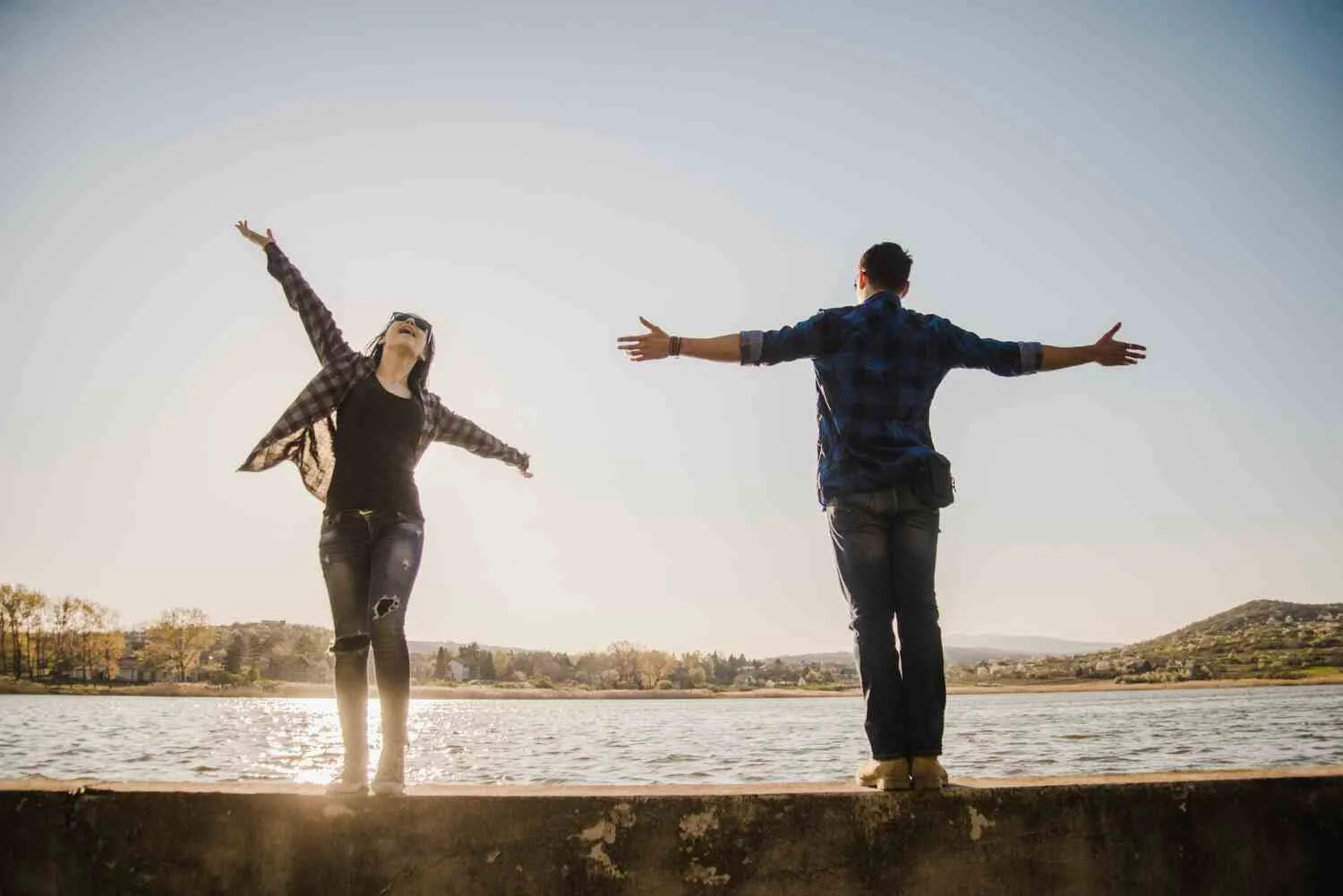 Two people standing by a lake with arms outstretched, embracing the moment. The scene, filled with sunlight and nature, symbolizes the impact of Life Experiences on mental health and well-being. Two people standing by a lake with arms outstretched, embracing the moment. The scene, filled with sunlight and nature, symbolizes the impact of Life Experiences on mental health and well-being.
