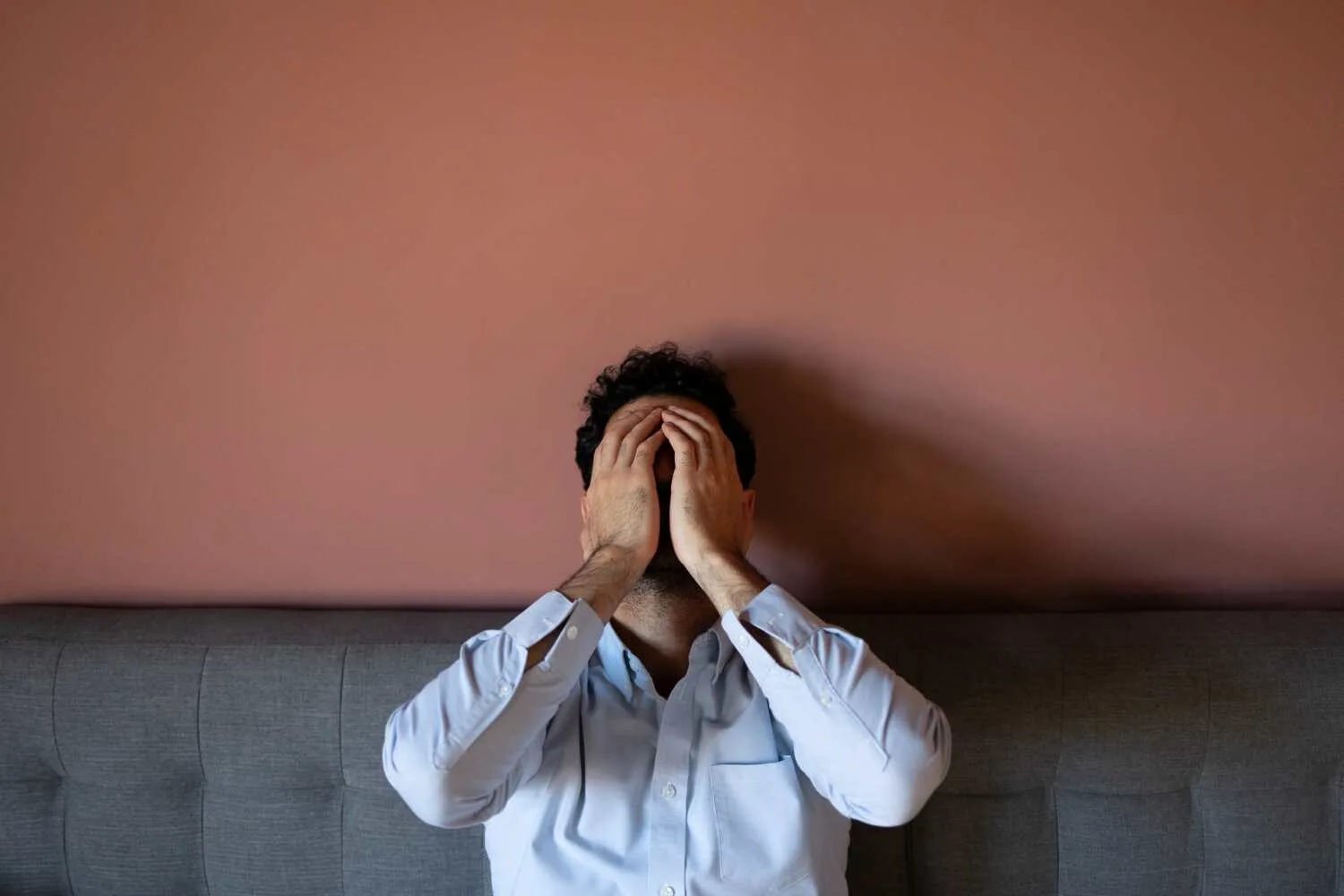 Man sitting on a couch with hands covering his face, expressing distress and overwhelm, illustrating the effects of Anxiety Disorders. Man sitting on a couch with hands covering his face, expressing distress and overwhelm, illustrating the effects of Anxiety Disorders.
